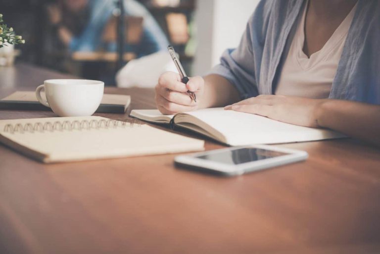 Femme écrivant dans un carnet avec une tasse de thé et une tablette