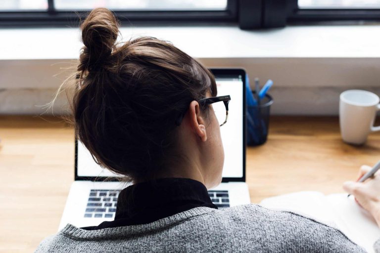 Femme prenant des notes tout en utilisant un ordinateur portable