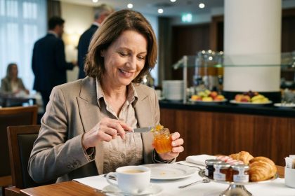 Femme habillee delicatement tartinant de la confiture d'abricot sur un croissant au petit déjeuner
