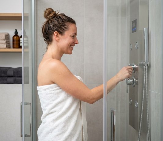 La colonne de douche hydromassante : plus de confort dans votre salle de bain Femme souriante dans la douche hydromassage moderne