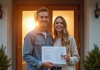 Jeune couple heureux devant leur maison avec clés et documents