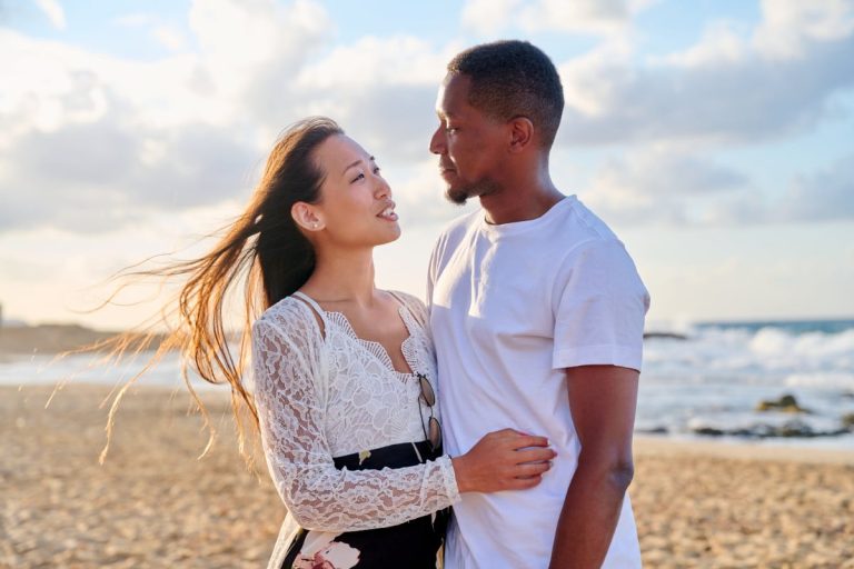 jeune couple s'enlaçant sur la plage avec un air pensif